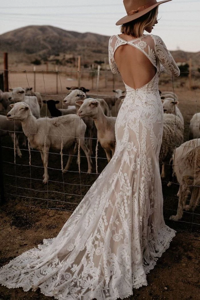 blonde woman standing next to sheep wearing dress made of lace with bare back bohemian style wedding dresses