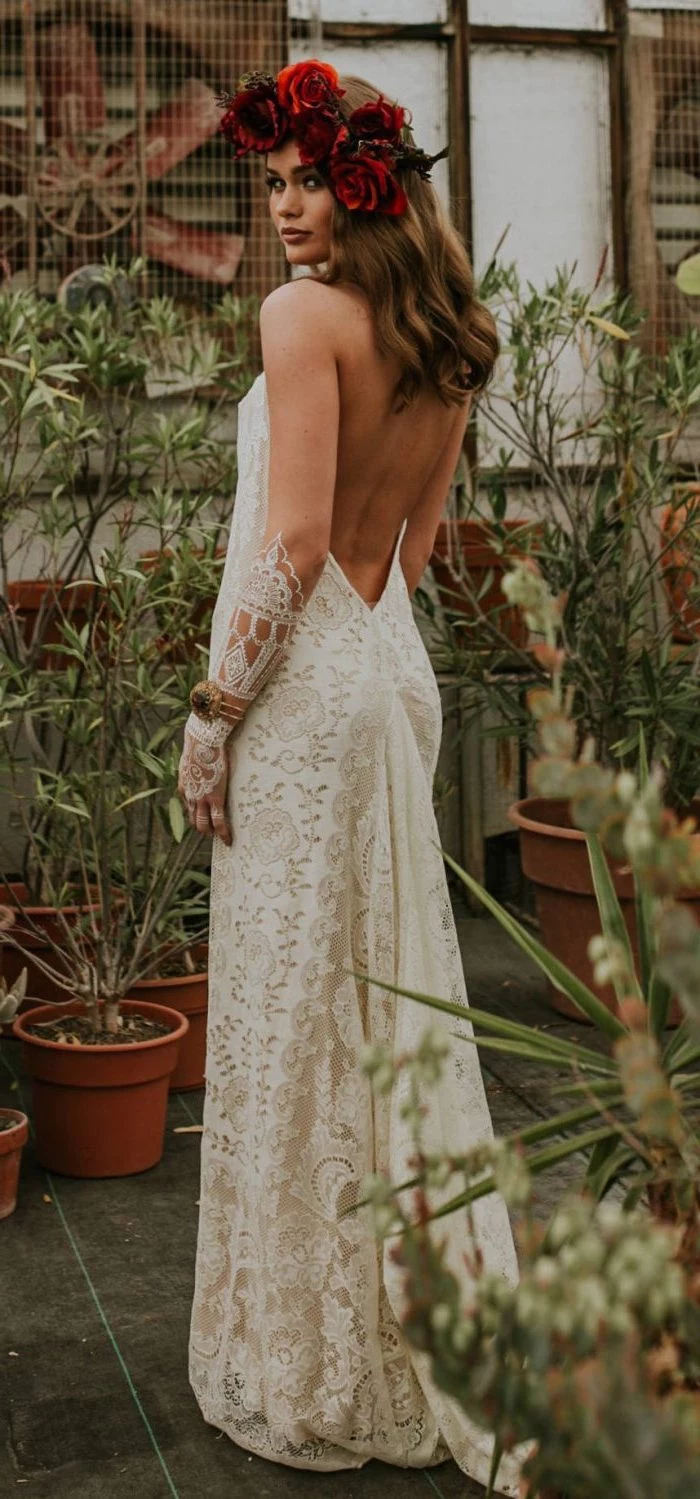 boho beach wedding dress woman with medium length light brown wavy hair wearing floral crown made of red roses long lacy dress with bare back
