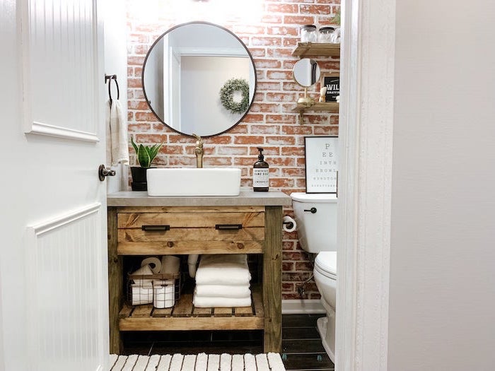 brick wall behind wooden vanity with open shelving round mirror above it farmhouse bathroom wall decor wooden shelves above the toilet