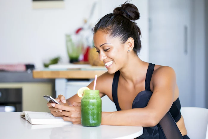 brunette woman sitting on a chair next to table best detox cleanse green smoothie book on the table