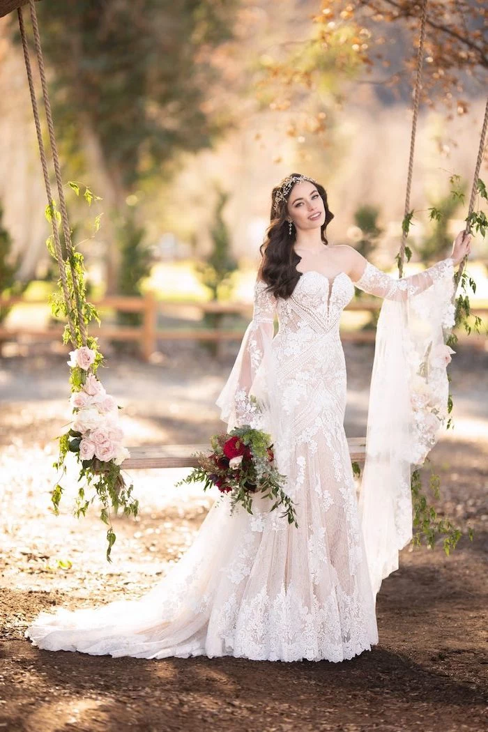 brunette woman wearing all lace dress with long sleeves bohemian wedding dress standing next to swing with flowers