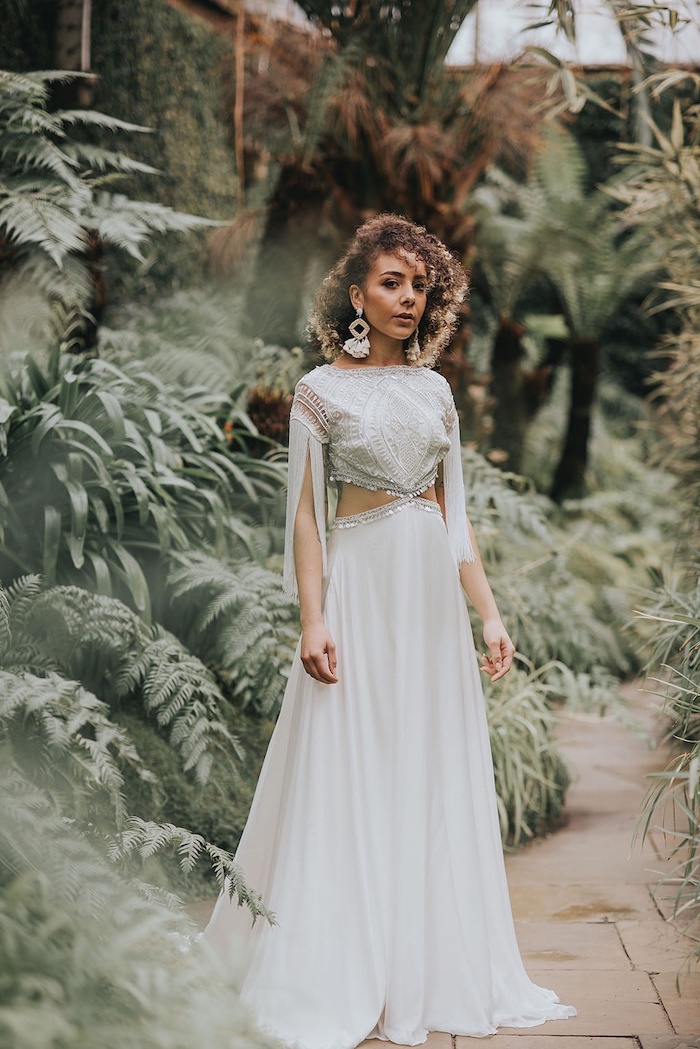 brunette woman with shoulder length curly hair wearing long flowy wedding dress with lacy top and bottom made of tulle