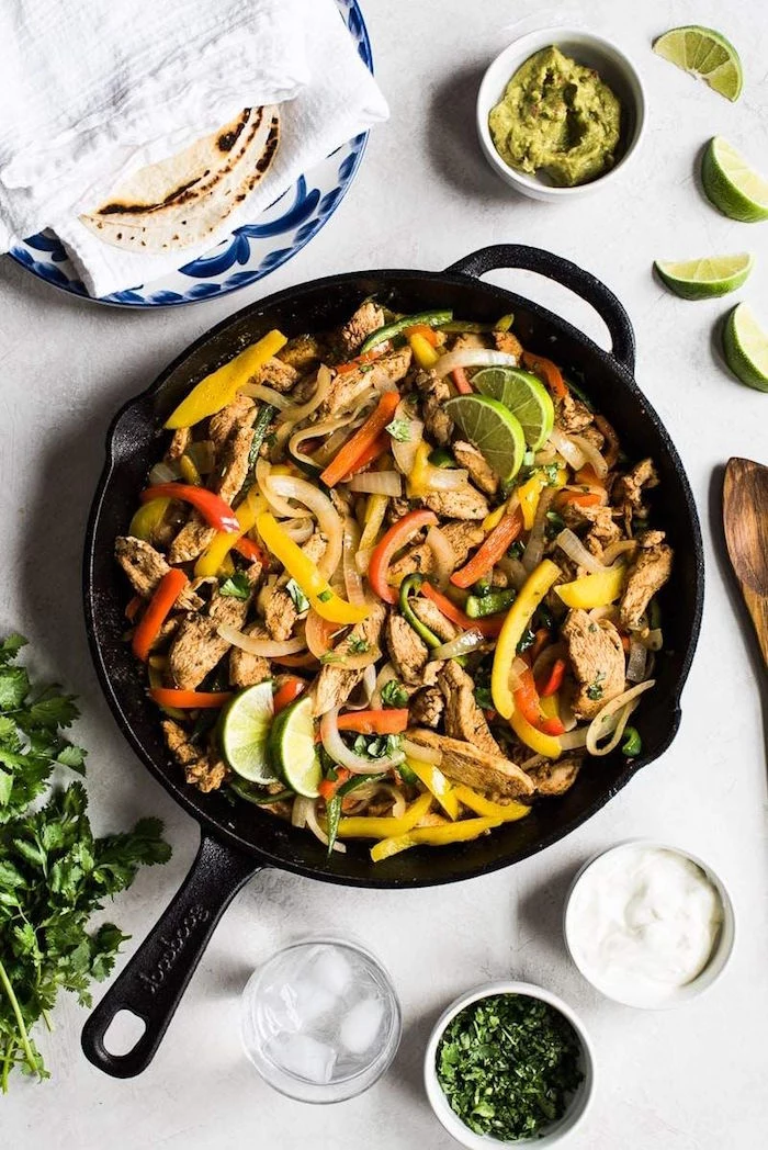 chicken fajitas cooked in black dish mexican food recipes with peppers onion garnished with lime slices and chopped fresh parsley