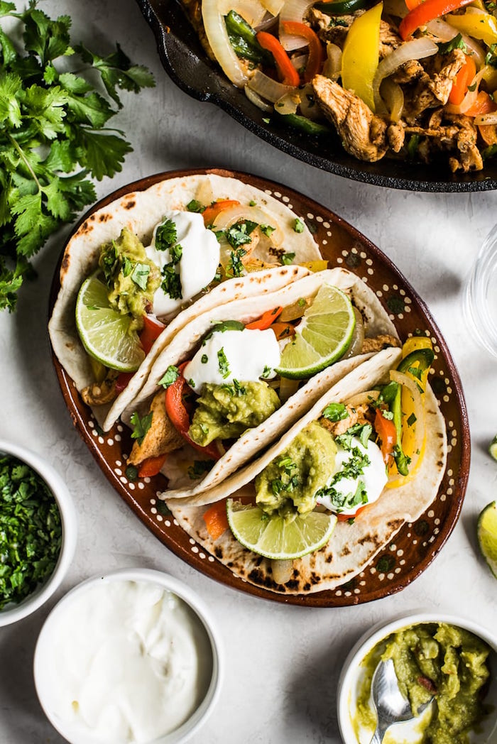 chicken fajitas inside tacos with guacamole sauce mexican food recipes lime slices and fresh parsley for garnish