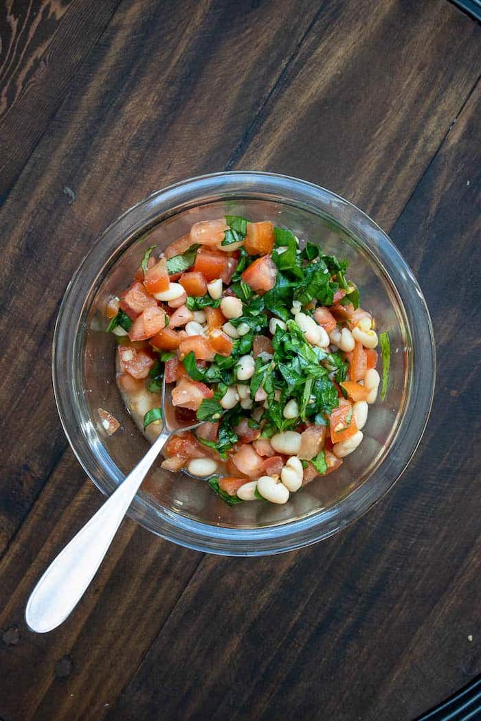 chopped tomatoes beans basil inside glass bowl with spoon on the side vegan appetizer recipes placed on wooden surface