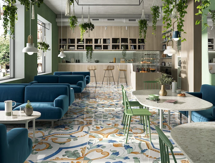 colorful tiles with floral print on the floor of restaurant with blue velvet sofas green chairs floor tiles plants hanging from the ceiling