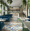 colorful tiles with floral print on the floor of restaurant with blue velvet sofas green chairs floor tiles plants hanging from the ceiling