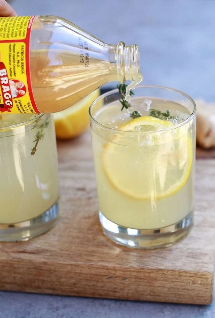 detox drinks for weight loss apple cider with lemon slices garnished with herbs poured inside glass placed on wooden cutting board