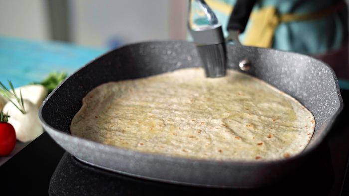 easy mexican dishes tortilla covered with butter cooking in black grill pan placed on blue wooden surface
