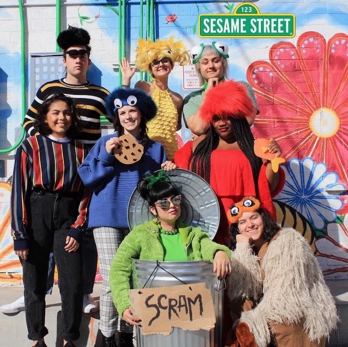 eight people dressed as the characters from sesame street trio halloween costumes posing in front of wall with grafitti
