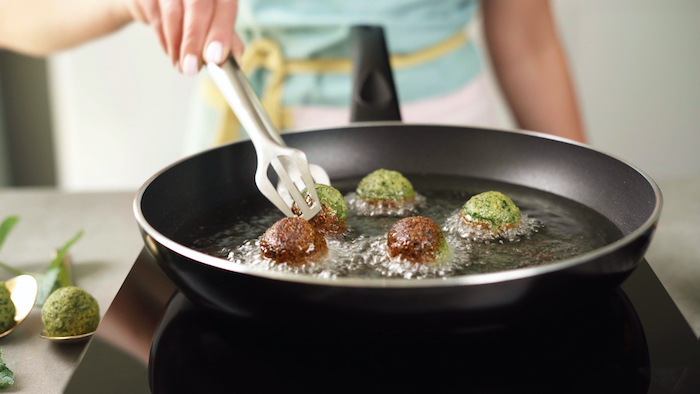 falafels being turned into oil in black sauce pan with metal tongs vegan hors d oeuvres one half fried