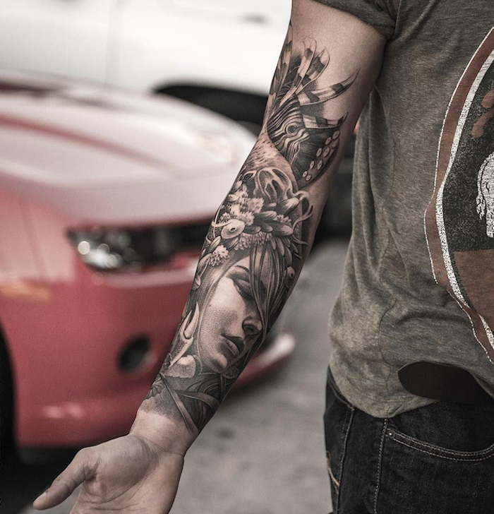 female face surrounded by flowers leaves feathers half sleeve forearm tattoo on man wearing jeans gray t shirt tattoo designs for men