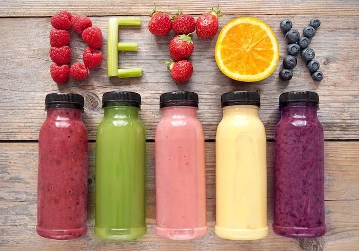 five bottles filled with smoothies in different colors how to detoxify your body detox written with fruits above them