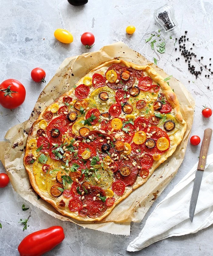 flatbread baked with different kinds of tomatoes olives pine nuts chopped basil vegan bites placed on white surface