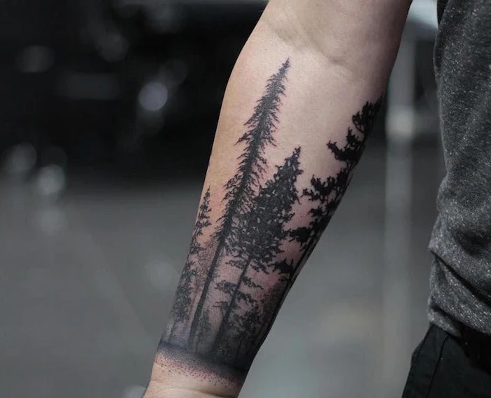 forest landscape with tall trees wrap around forearm tattoo small tattoo ideas for men wearing black jeans gray t shirt