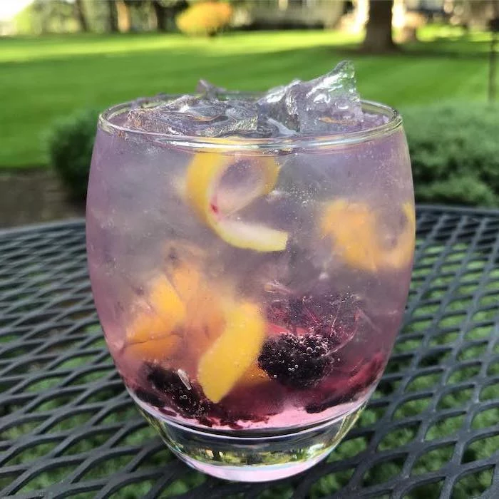 glass filled with blackberry lemonade filled with ice detox drinks placed on black garden table