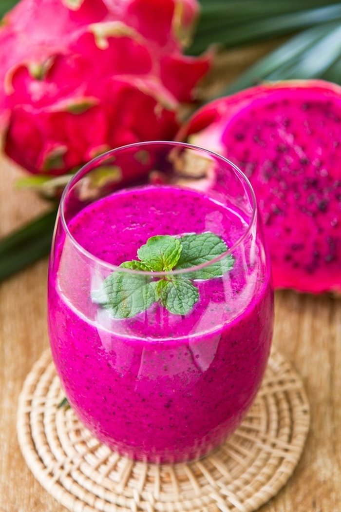 glass filled with dragonfruit smoothie garnished with fresh mint leaves what is detox placed on wooden surface