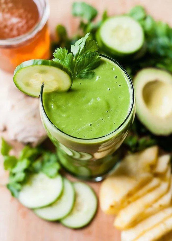 glass filled with green smoothie best detox cleanse for weight loss garnished with cucumber slice and fresh parsley vegetables around it