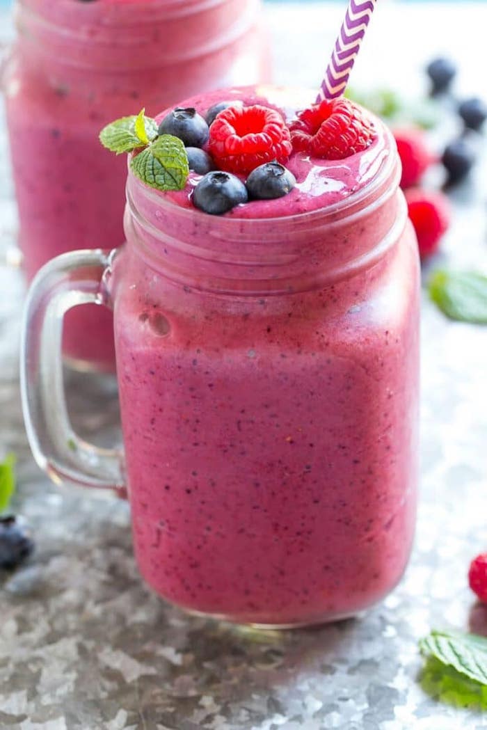 glass filled with red smoothie what is detox garnished with raspberries blueberries and fresh mint leaves