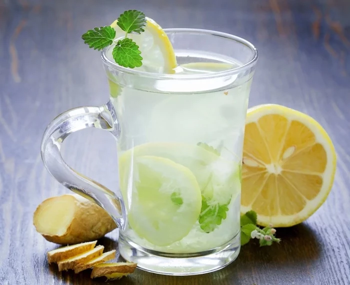 glass filled with water with lemon slices mint leaves ginger and lemon on the side what is detox placed on wooden surface