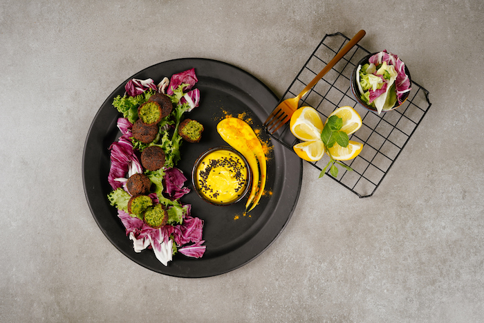 green falafels recipe vegan finger food placed on kale leaves on black plate with a dip in small black bowl on granite surface