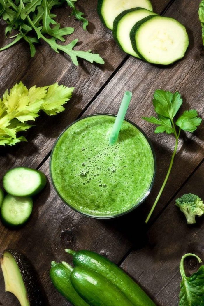 green smoothie inside a glass placed on wooden surface detox drinks different green vegetables herbs around it