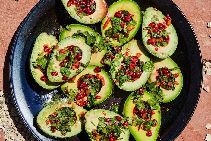 halved avocados filled with chopped parsley pomegranate seeds arranged on black plate vegan appetizers