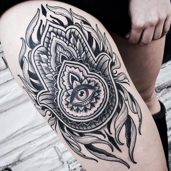 hamsa hand with all seeing eye surrounded by leaves tattoos with deep meaning black and white thigh tattoo