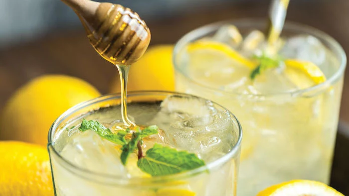 honey being poured into glass with lemonade ice and mint leaves detox drinks lemons on the side