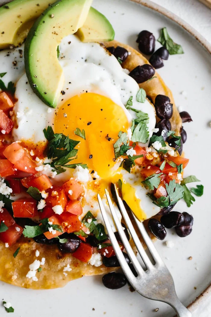 huevos rancheros on white plate mexican dinner ideas with chopped tomatoes black beans parsley crumbled feta cheese