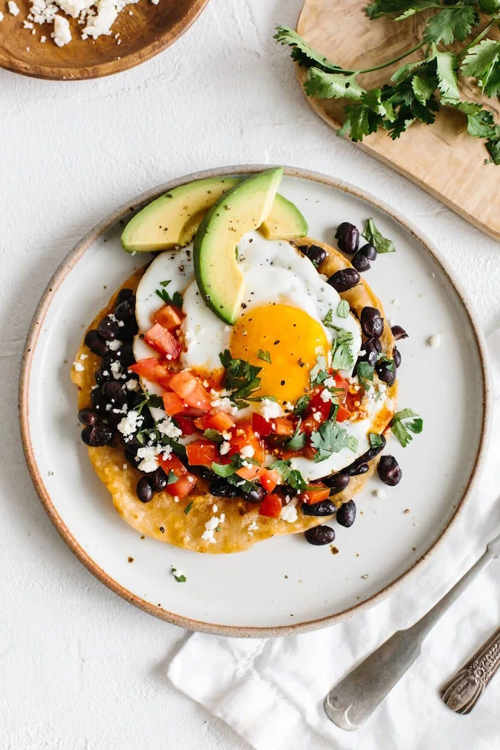 huevos rancheros with tomatoes black beans chopped parsley crumbled feta cheese mexican dinner ideas slices of avocado