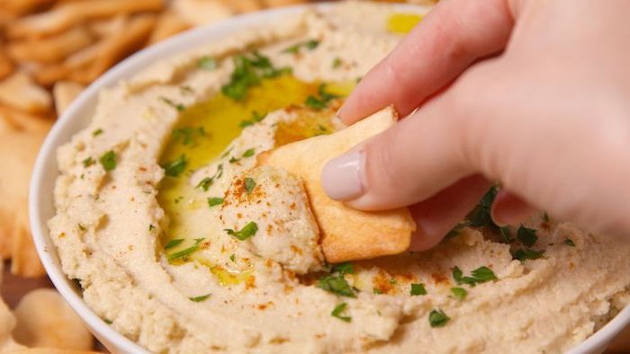 hummus garnished with olive oil chopped parsley red pepper powder vegan appetizers bread being dipped into it