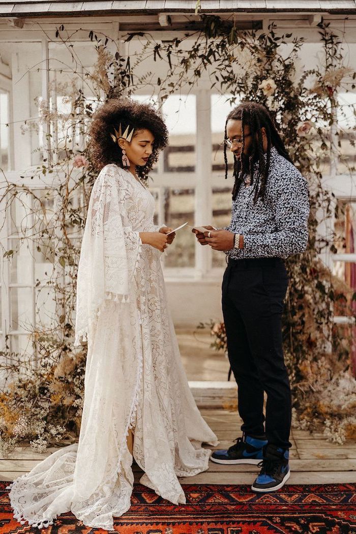 man and woman standing at the altar boho wedding dress woman wearing all lace white dress with wide sleeves man wearing black pants floral shirt