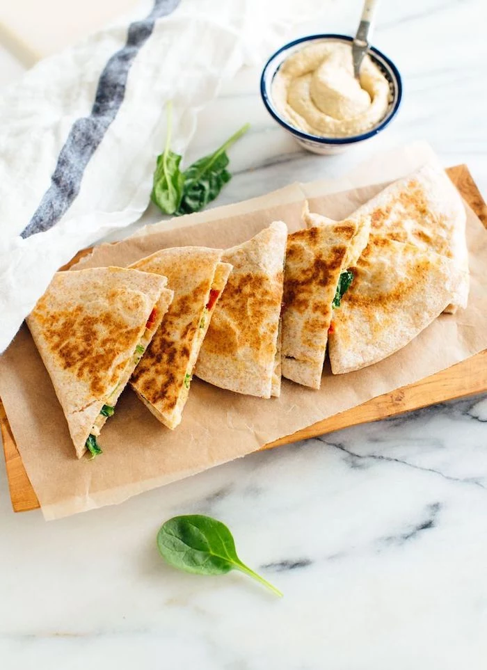 marble surface vegan hors d oeuvres paper lined wooden board with cut up quesadillas with hummus and spinach
