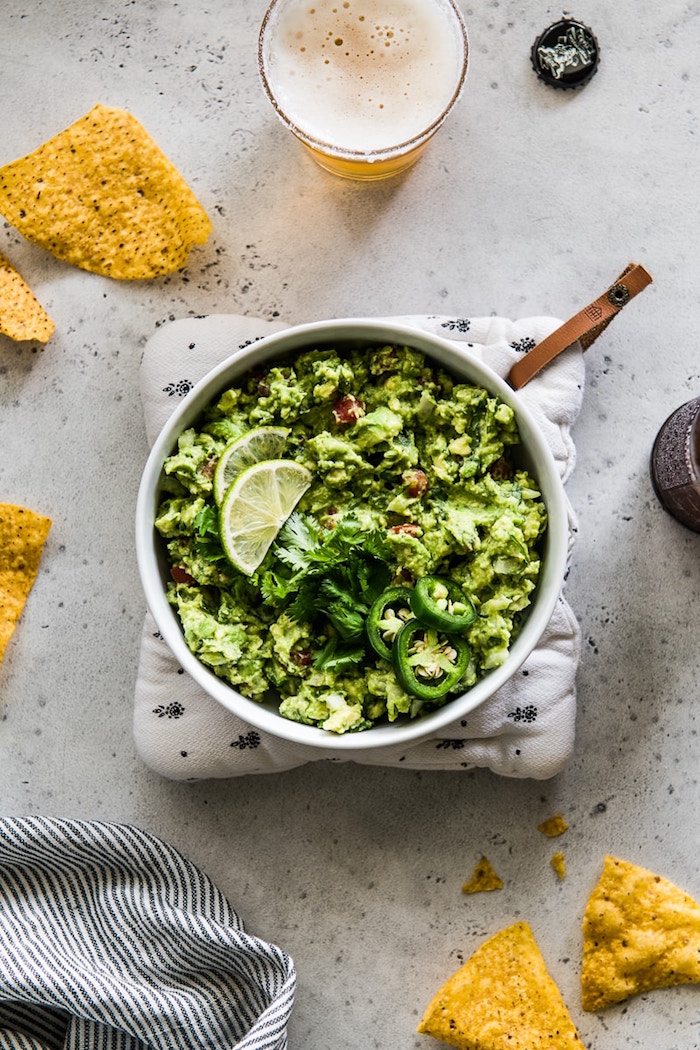 mexican dinner ideas guacamole inside white ceramic plate garnished with lime slices cilantro and chopped jalapenos