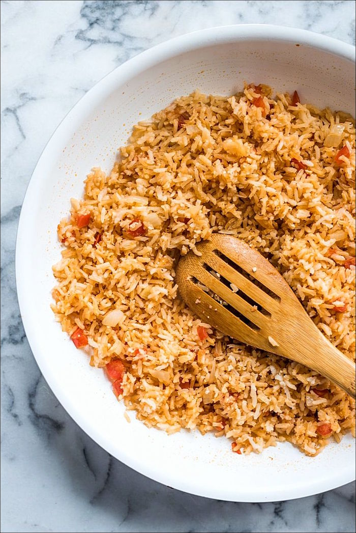 mexican rice with peppers in white ceramic bowl with wooden spatula authentic mexican recipes placed on marble surface