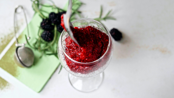 milk with chia seeds topped with mashed raspberries with chia seeds inside wine glass placed on white surface vegan bites