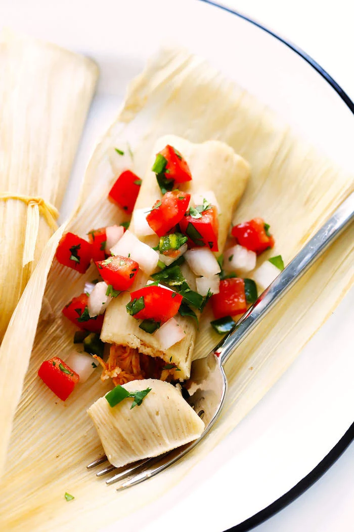 popular mexican food tamales garnished with chopped tomatoes onion parsley placed on white plate