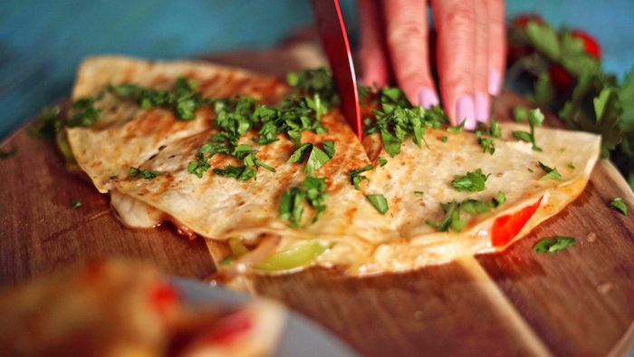 quesadilla placed on round wooden cutting board garnished with chopped parsley easy mexican dishes being cut into triangles