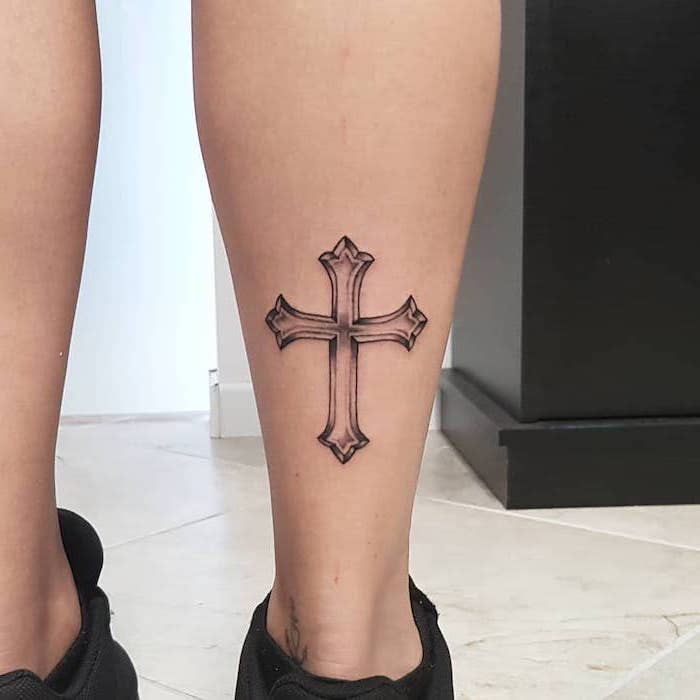 silhouette of a cross tattooed on the back of the leg of woman wearing black sneakers tattoos that mean strength