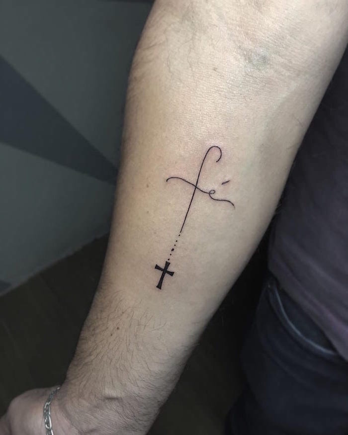 simple tattoos for men forearm tattoo of small cross fe written above it in cursive font on man wearing jeans dark t shirt