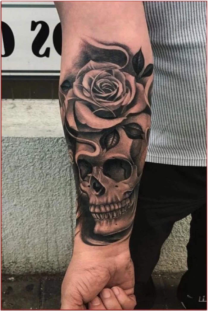 skull with rose forearm tatttoo on man wearing black jeans black and white striped shirt small tattoo ideas for men