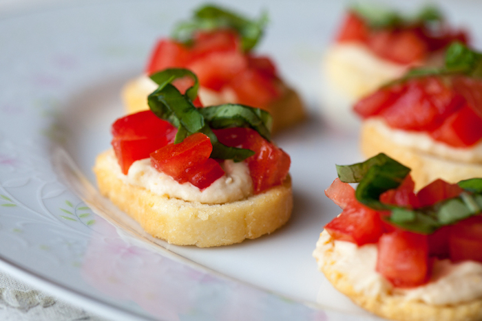 small bruschetinni with hummus chopped tomatoes and basil on top vegan party food arranged on white plate