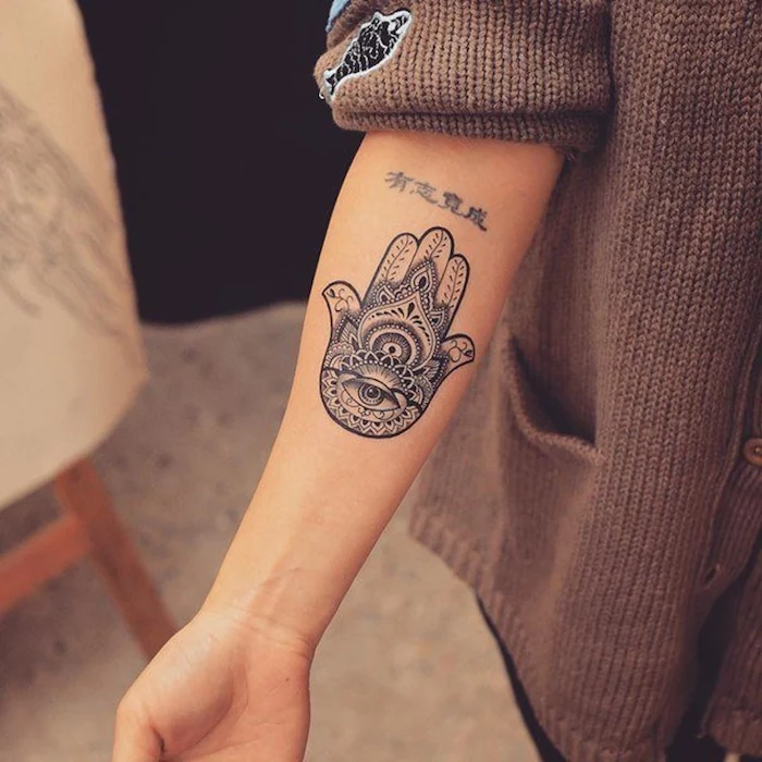 spiritual tattoos black and white hamsa hand forearm tattoo on woman dressed with brown knitted cardigan