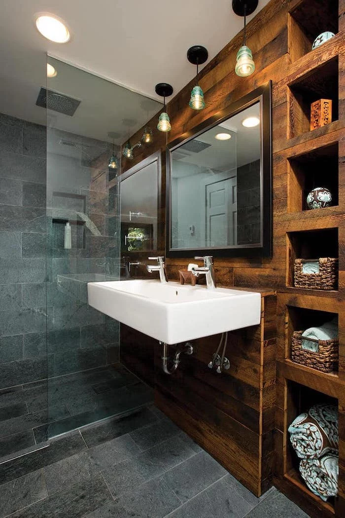 stone tiles on the floor and in the shower wooden wall with shelves around floating sink with two faucets rustic bathroom decor large mirror