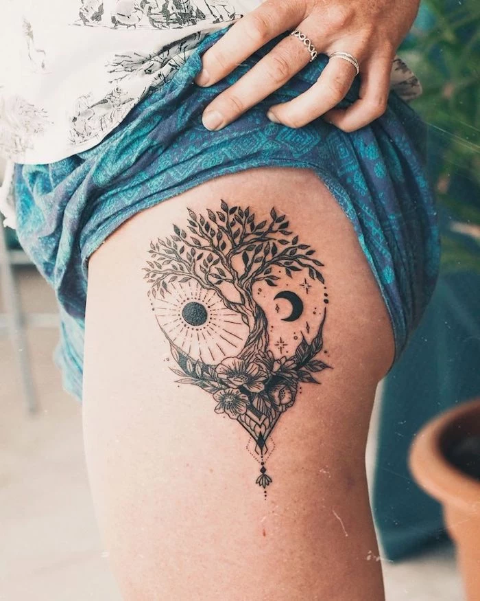 strength symbol tattoo tree of life tattoo with moon and sun on the side of the hip on woman wearing blue shorts