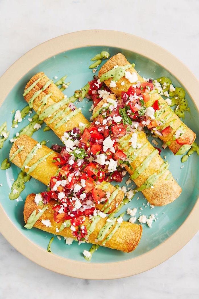 taquitos covered with salsa guacamole and crumbled feta cheese mexican dishes placed on blue plate