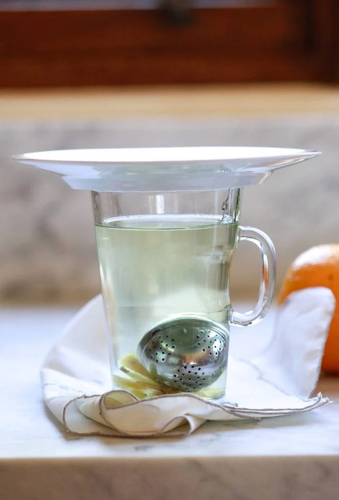 tea infuser inside a glass filled with water covered with plate best cleanse for weight loss placed on white cloth