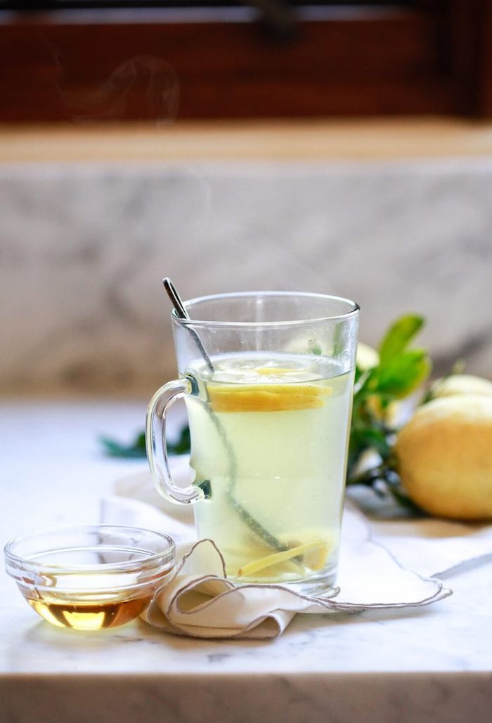 tea inside a glass with spoon lemon slices inside best cleanse for weight loss small bowl with honey on the side