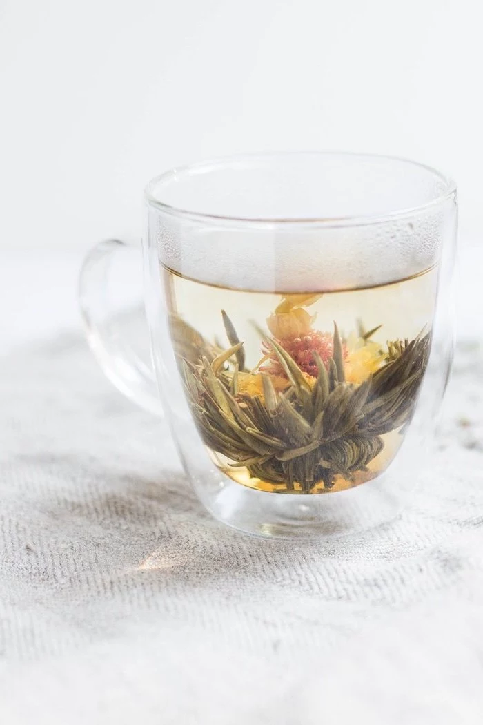 tea with different herbs inside a glass how to detox your body placed on white surface
